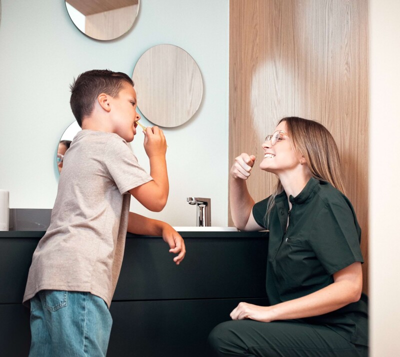 Frau Elisa Riekert (rechts im Bild) macht einem kleinen Jungen vor, wie man sich die Zähne richtig putzt.