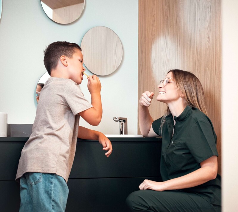 Frau Elisa Riekert (rechts im Bild) macht einem kleinen Jungen vor, wie man sich die Zähne richtig putzt.