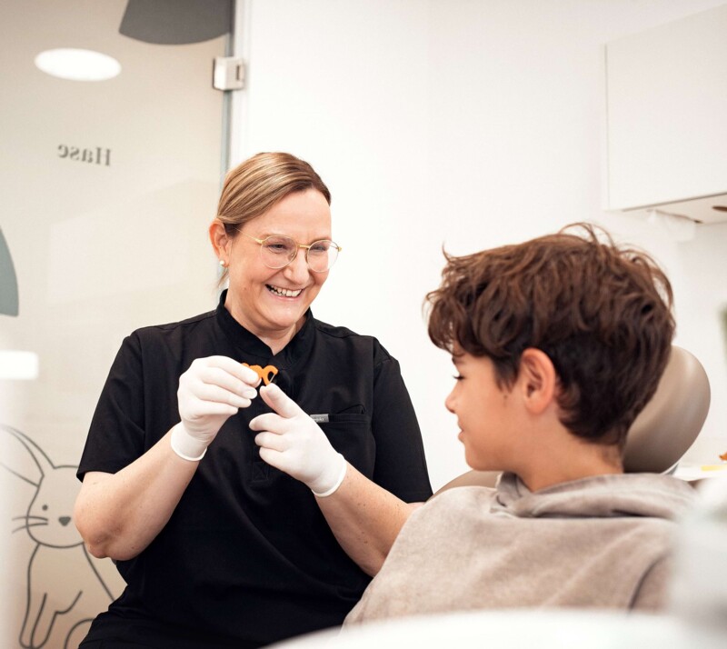 Frau Schönleber zeigt einem jungen Patienten, wie man Zahnseide richtig benutzt.